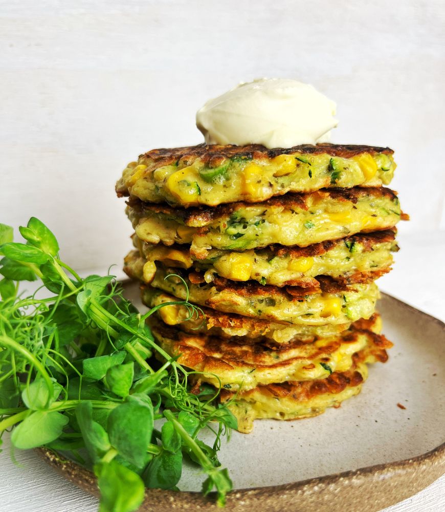 Zucchini & Corn Fritters stacked up on a plate with salad and a dollop of sour cream