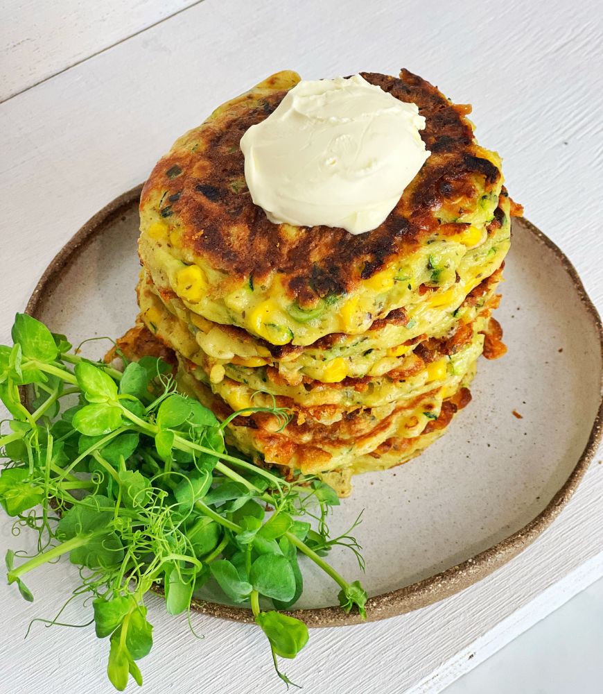 zucchini fritters on a plate with salad leaves and topped wtih sour cream