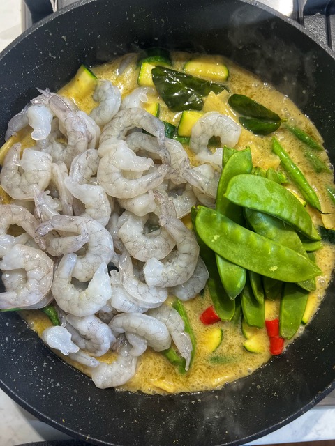 PRAWNS AND SNOW PEAS ADDED TO GREEN CURRY SAUCE COOKING IN A PAN