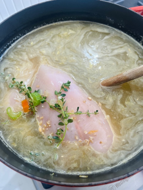 pot filled with stock, herbs and chicken breast fillet with wooden spoon in pot
