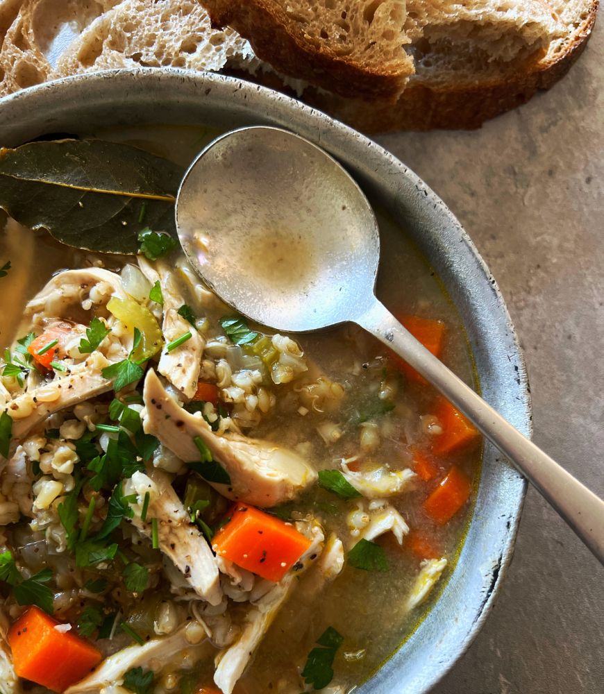 grain and chicken soup in an old saucepan with silver spoon on top. bread in background
