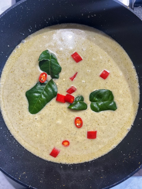 green curry sauce in pan with kaffir lime leaves and red chilli slices