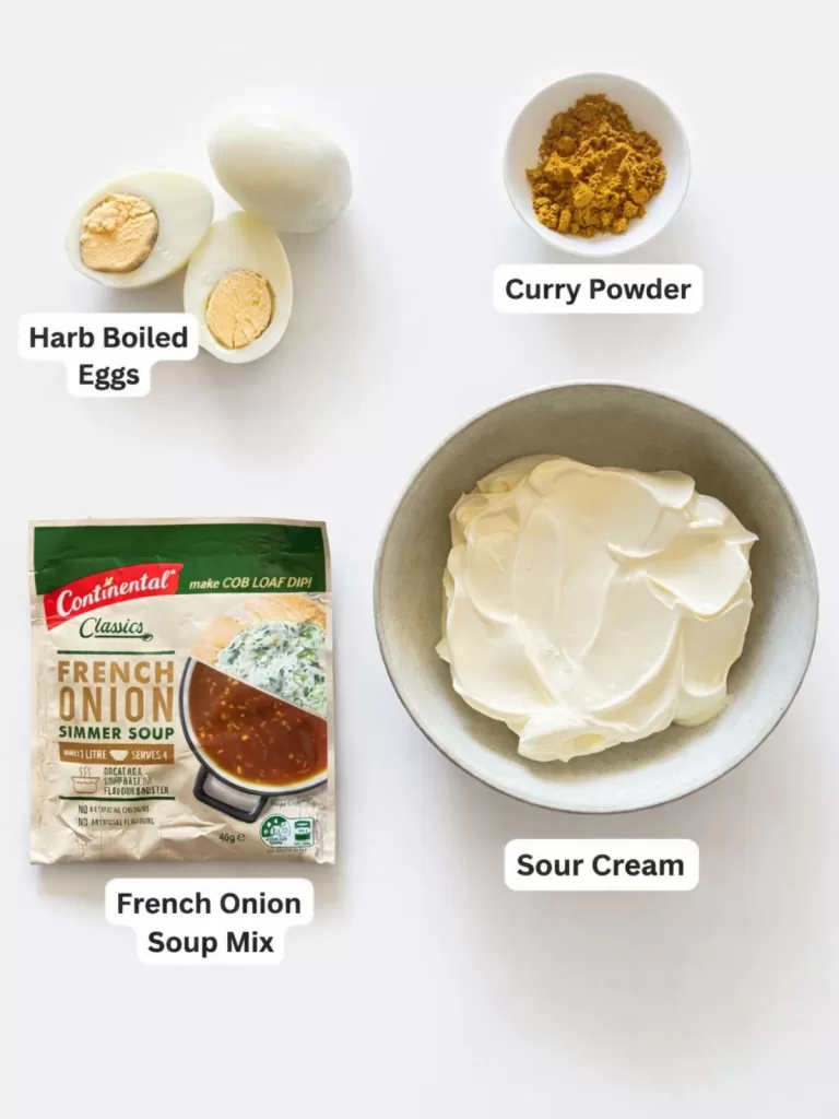 Ingredients for curried egg dip on a white background including hard boiled eggs, curry powder, sour cream in a bowl and a packet of French onion soup mix.
