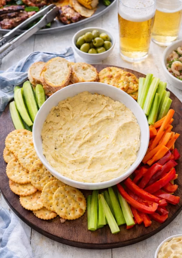 curried egg dip in a white bowl surrounded by crackers and vegetable crudites.