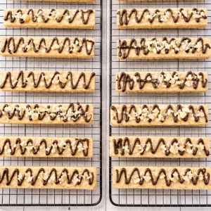 Macadamia shortbread fingers with chocolate drizzle on cooling racks