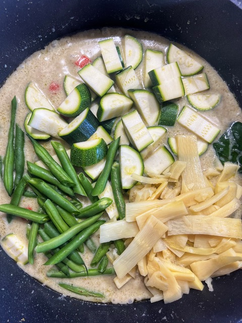 vegetables added to green curry sauce in pan