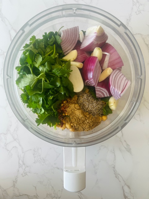 food processor bowl with herbs, onion, chickpeas & spices inside of it