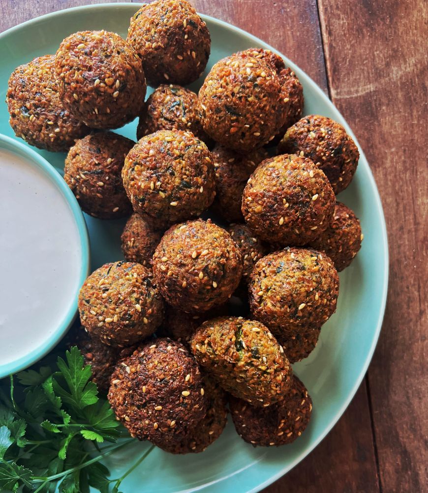 falafels on a green plate with tahini dipping sauce close up image