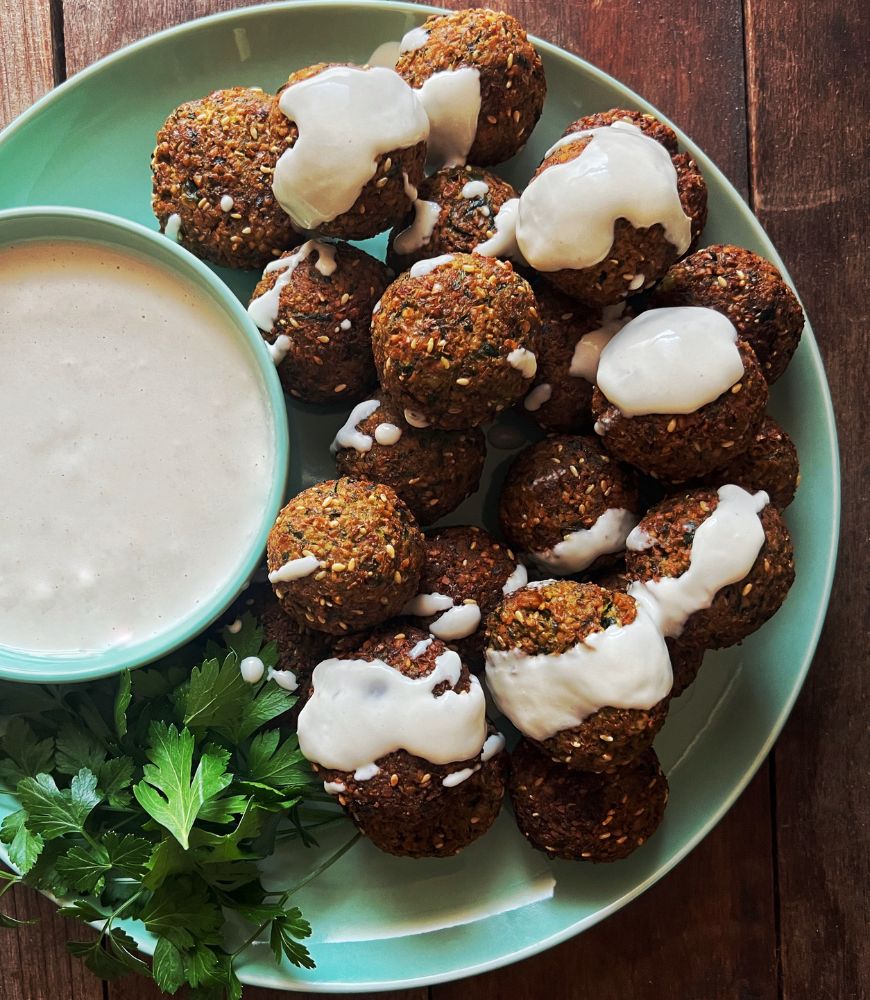 falafels drizzled with tahini dipping sauce on a green plate and dark wood background