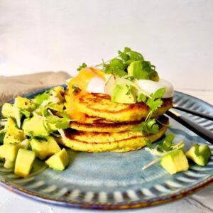 CORN FRITTER STACK WITH AVOCADO SALSA AND POACHED EGG ON BLUE PLATE