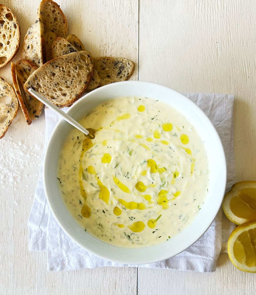 Greek Tzatziki dip in white bowl on white napkin on white board. Lemon cheeks and crackers around it.
