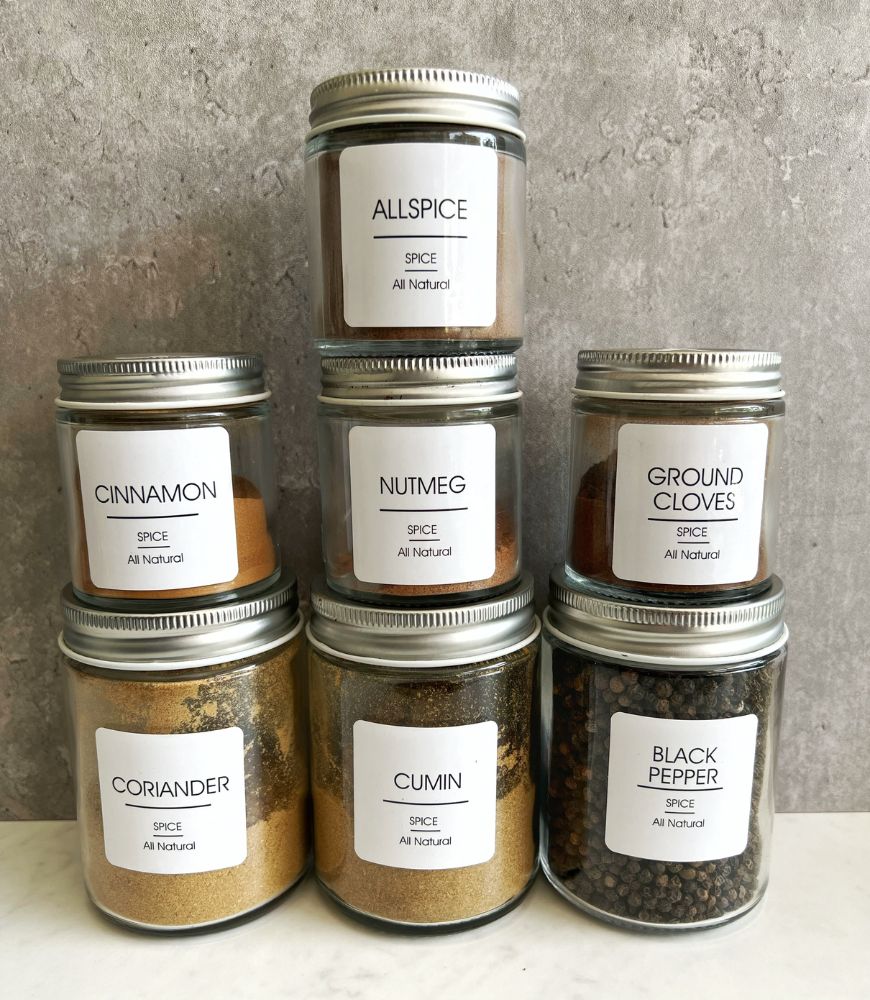 7 SPICE JARS WITH LABELS STACKED UP ON A GREY BACKGROUND