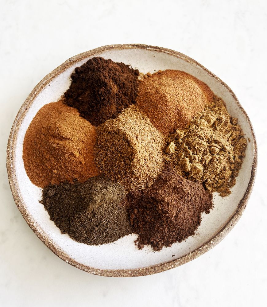 array of different spices piled in spots on a ceramic bone coloured plate, white background