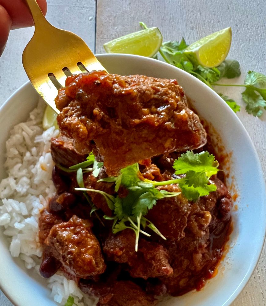 Piece of Mexican chilli beef on a fork close up with bowl of beef under it