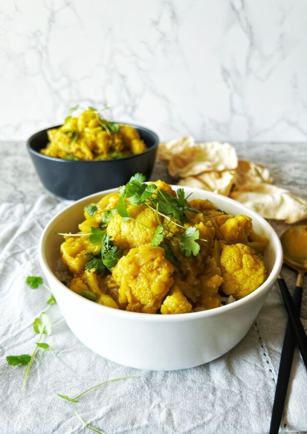 two bowls of lentil and cauliflower curry on grey background with herbs sprinkled over