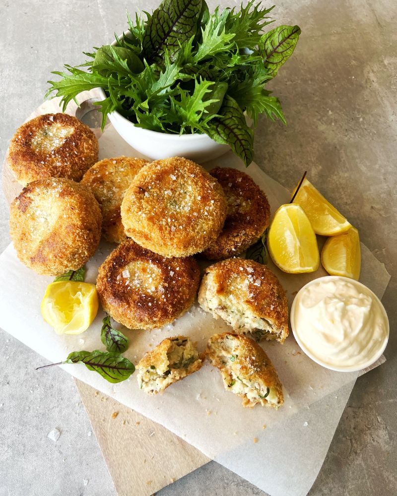 salmon & potato cakes on baking paper with green salad, lemon wedges and aioli