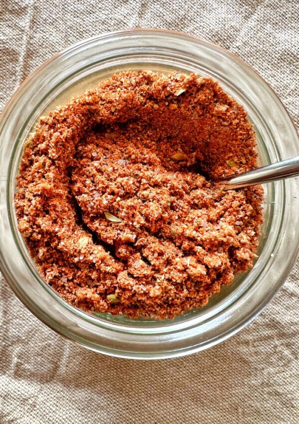 homemade taco seasoning in a glass jar with spoon on a beige cloth background