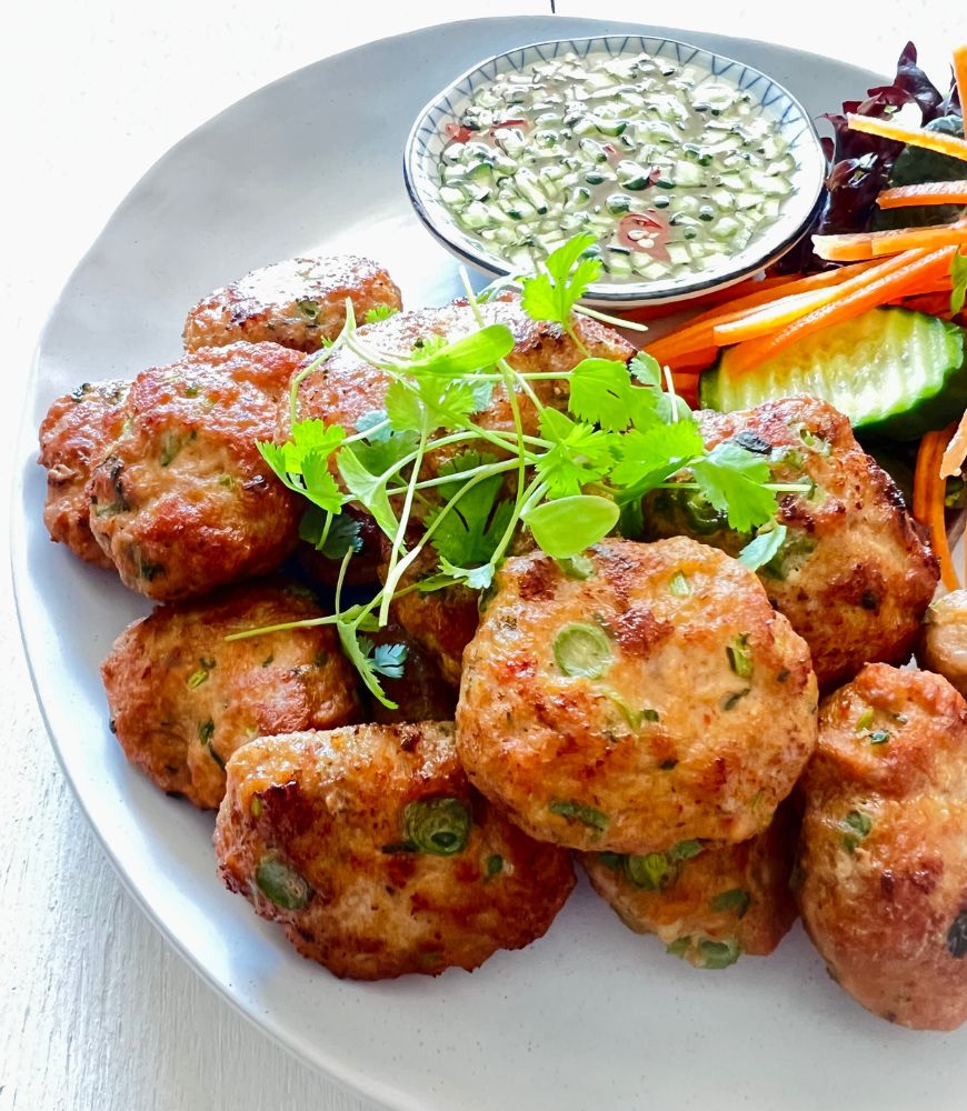 pork cakes on white plate with vegetables, garnished with coriander leaves