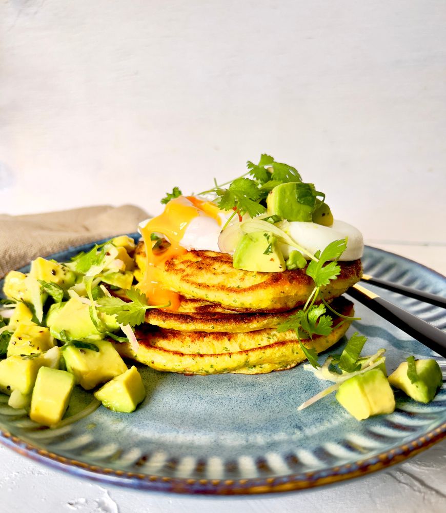 three corn fritters with avocado salsa and poached egg on blue plate