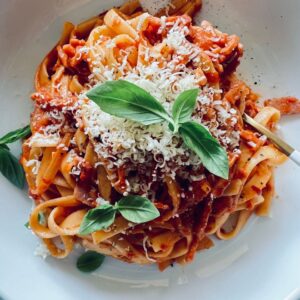 creamy tomato, chilli & bacon fettuccini in a white bowl with parmesan and basil leaves