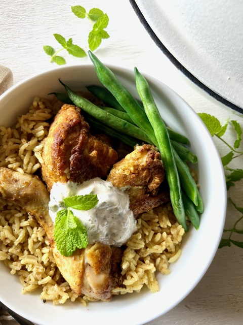 chicken and rice in a bowl with napkin, fork, spoon, mint leaves and yoghurt