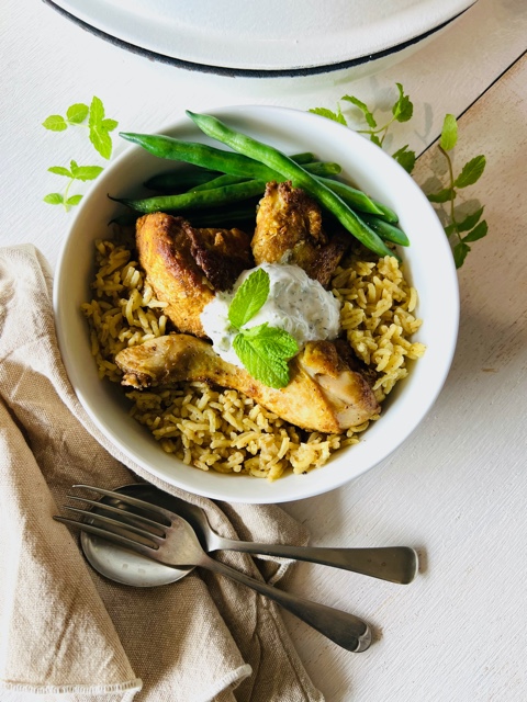 chicken and rice in a bowl with napkin, fork, spoon, mint leaves and yoghurt