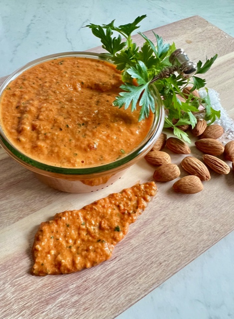 Red condiment in jar with parsley, almonds and some sauce smeared on the board