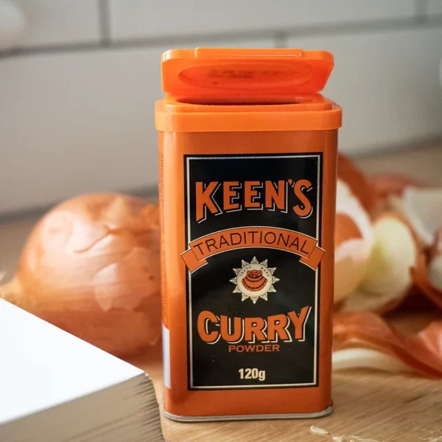 Keens curry powder container on bench with onions behind it