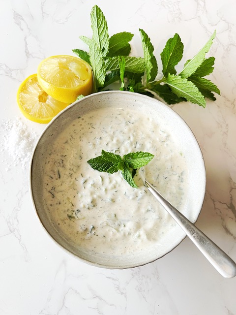 Cucumber & Mint Raita in a bowl with lemon and mint around the edge