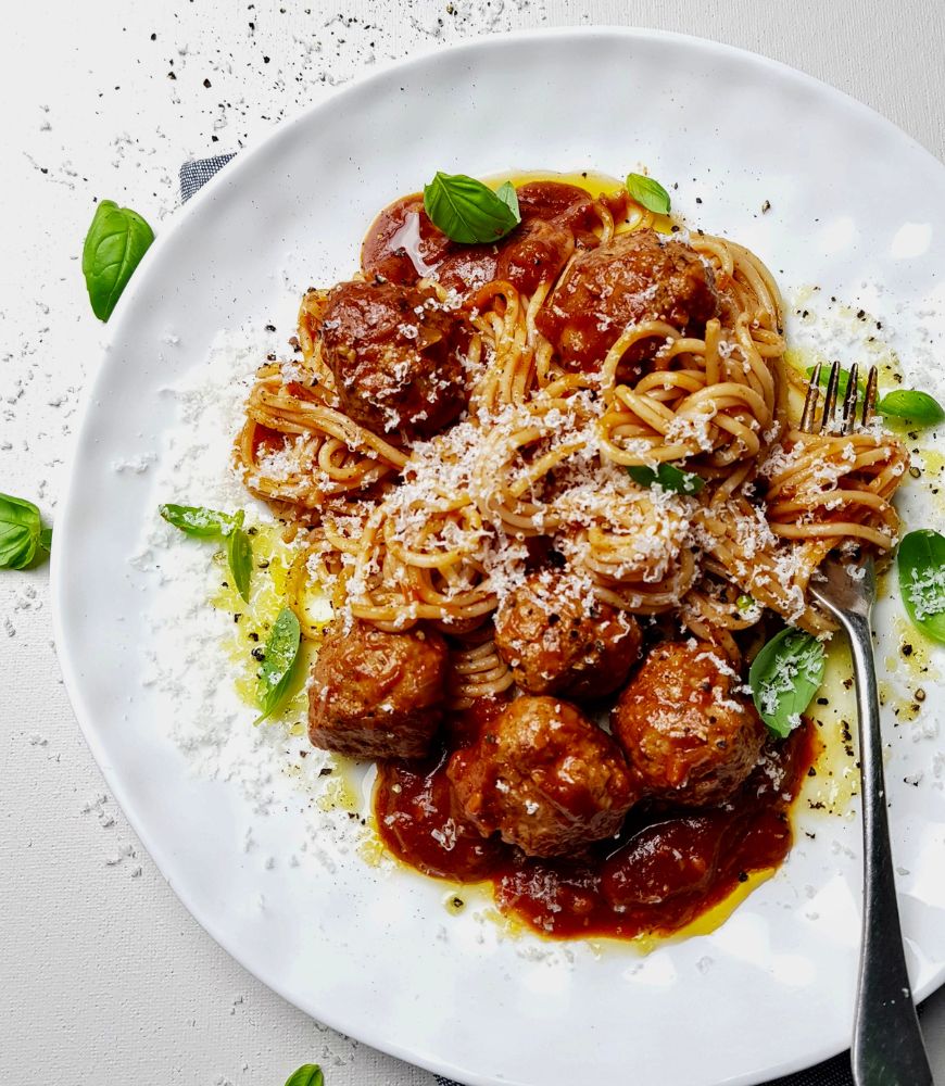 easy spaghetti & meatballs on white plate with basil and parmesan as garnish