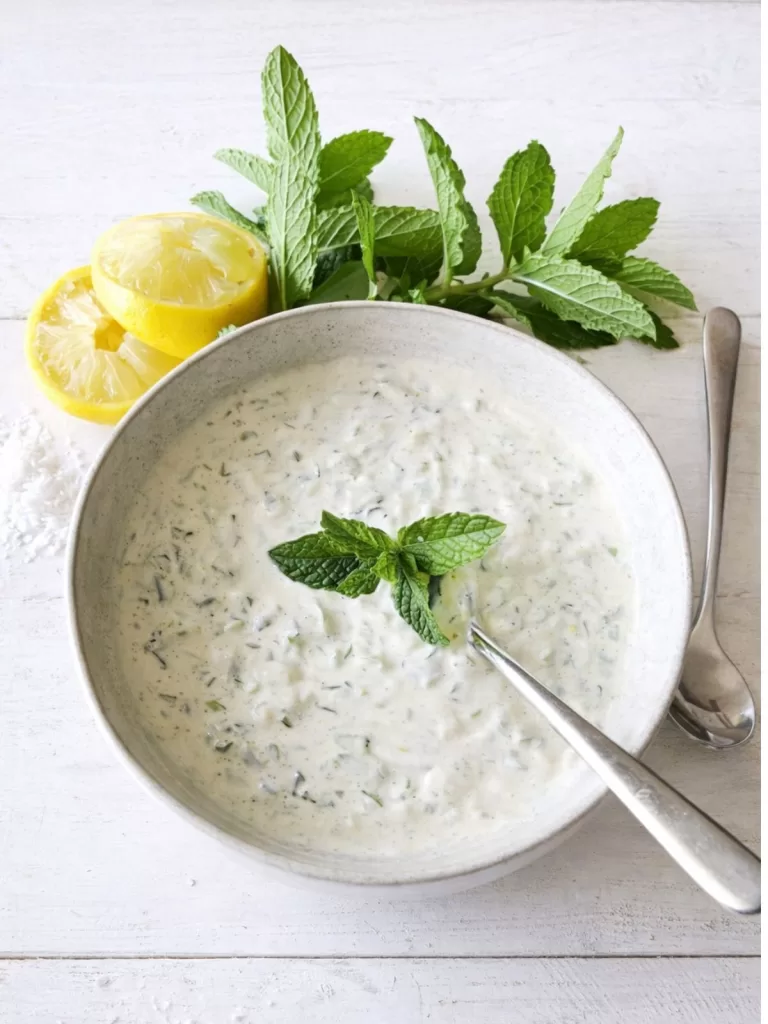 Cucumber & Mint Raita in a bowl with lemon and mint around the edge