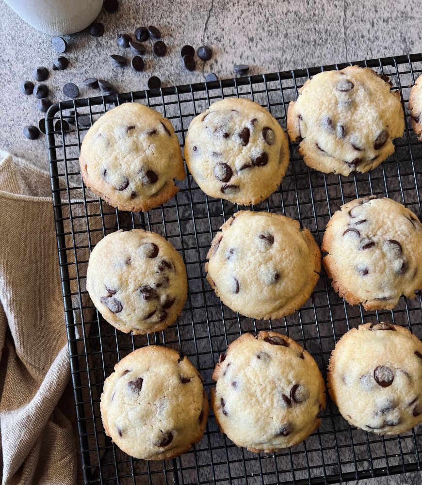 Basic Chocolate Chip Cookies on a wire rack with beige tea towel and choc chips scattered around