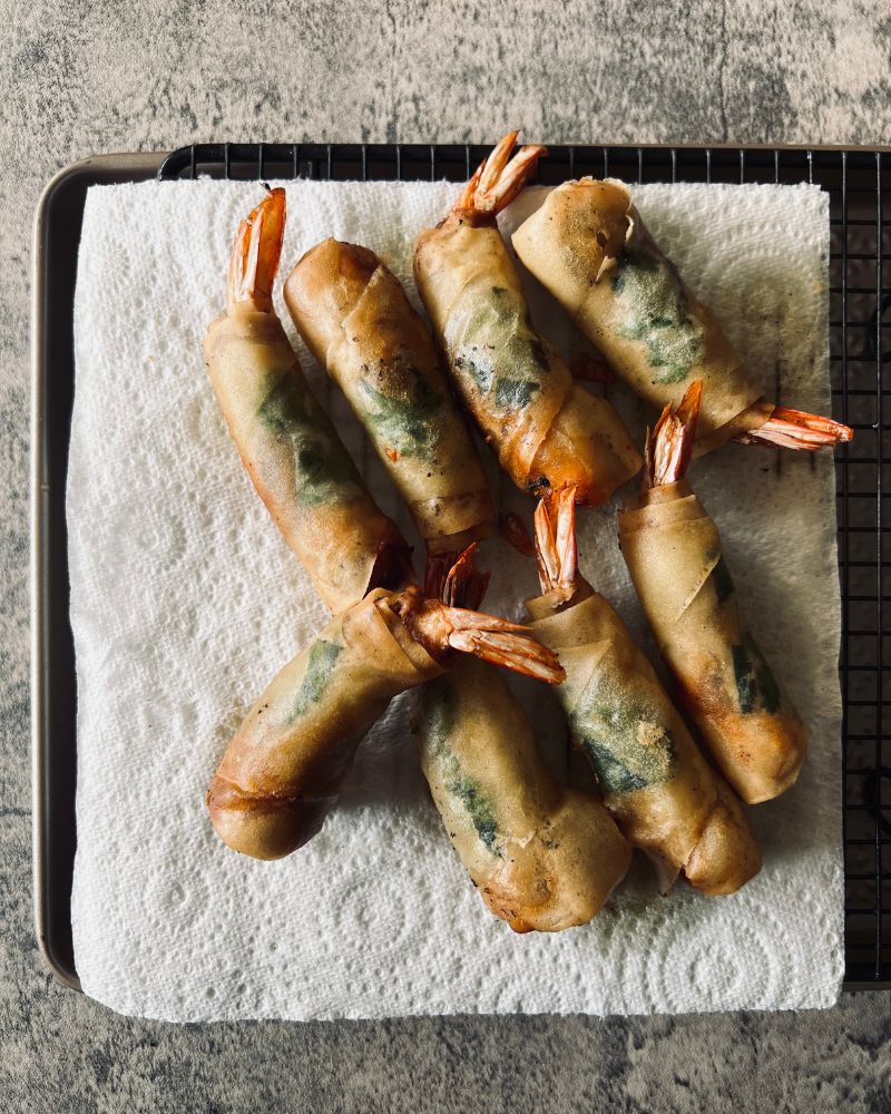 prawn spring rolls draining on paper towel over a wire rack