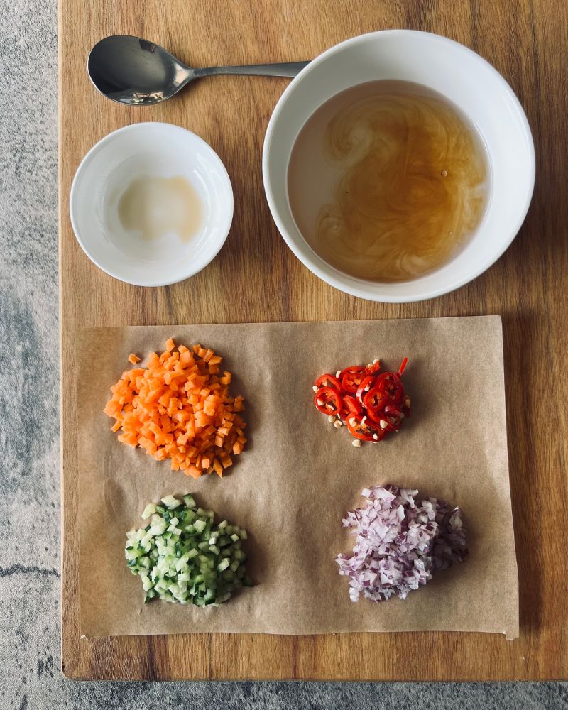 2 bowls and diced vegetables on a chopping board, one with fish sauce and one with vinegar mixture.