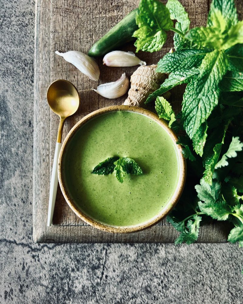 green chuntey in bowl on wood board with herbs, garlic and a spoon