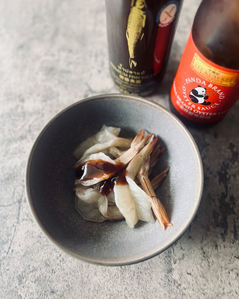 prawns in a grey bowl with fish and oyster sauce bottles in background