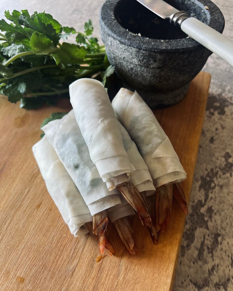 raw spring rolls on chopping board with mortar and pestle and coriander in background