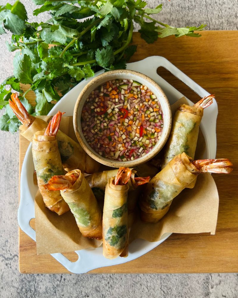 Thai spring rolls on wooden board with dipping sauce and coriander garnish