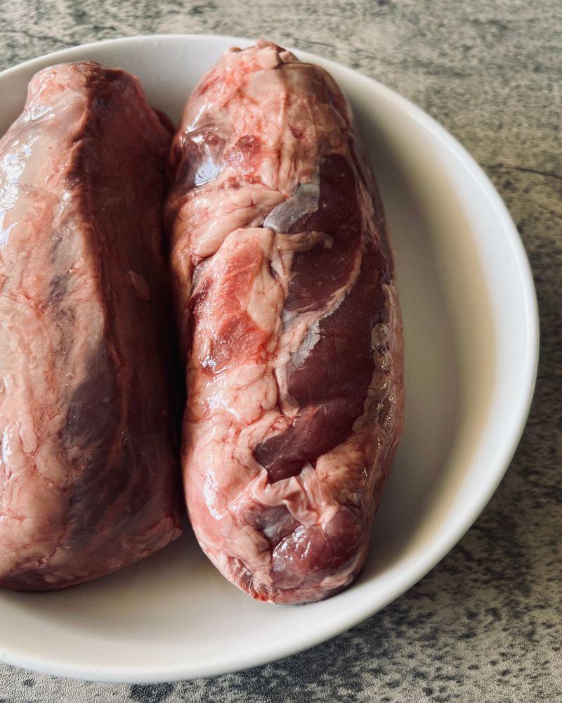 raw gravy beef whole shin in a white bowl on marble background. Close up image.