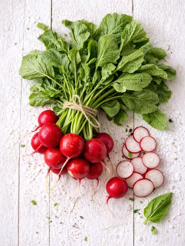 bundle of radishes with some also sliced on a white timber background.