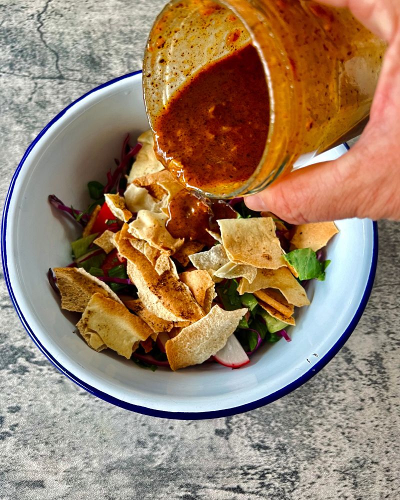 someone pouring dressing over a salad from a jar