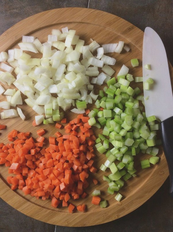 diced carrot, onion and celery on a wood board with knife