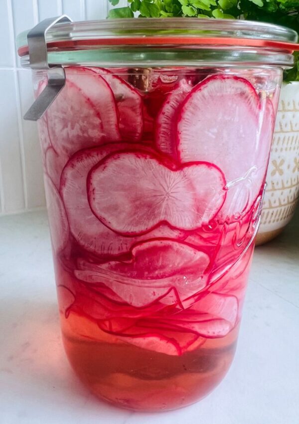thinly sliced radishes in a glass jar with pickling liquid