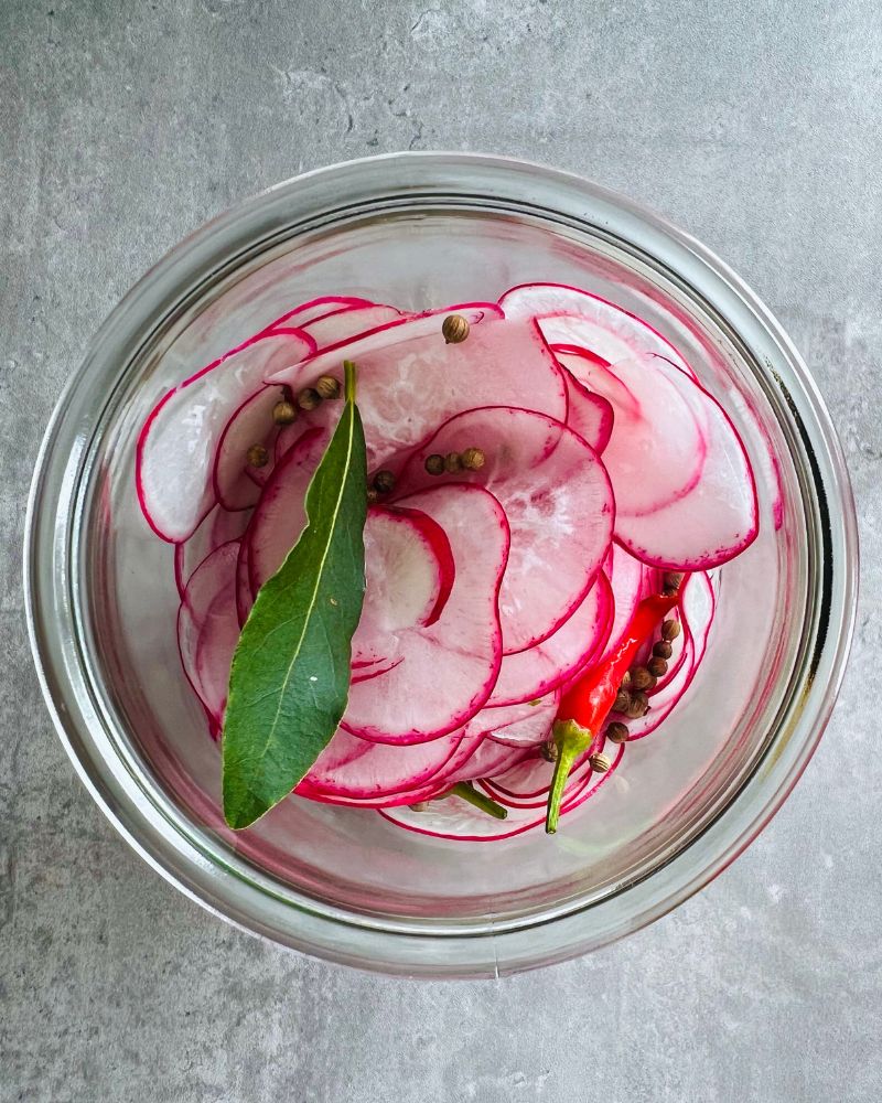 sliced radishes in a glass jar with chilies and bay leaf