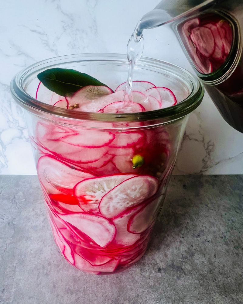 pouring pickling liquid over sliced radishes in a jar