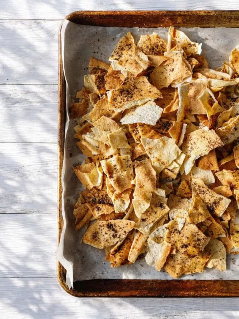 homemade pita crisps on a baking tray with white timber background.