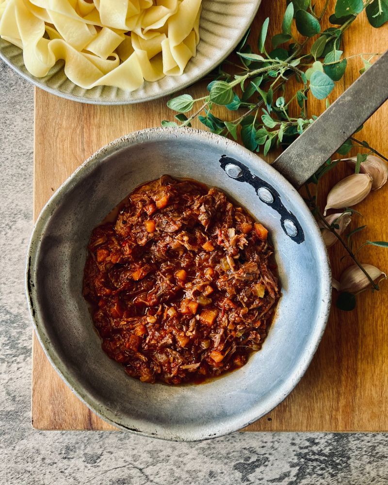 beef ragu in small saucepan on wooden board