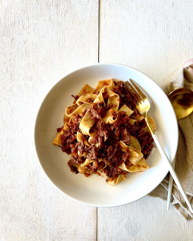 pasta with beef ragu sauce in white bowl on white wood background