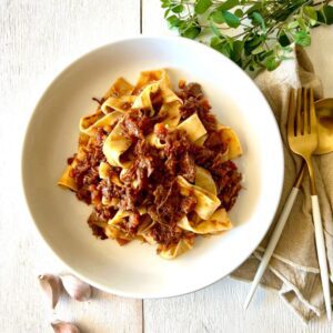 pasta with beef ragu in white bowl, white background, herbs and garlic