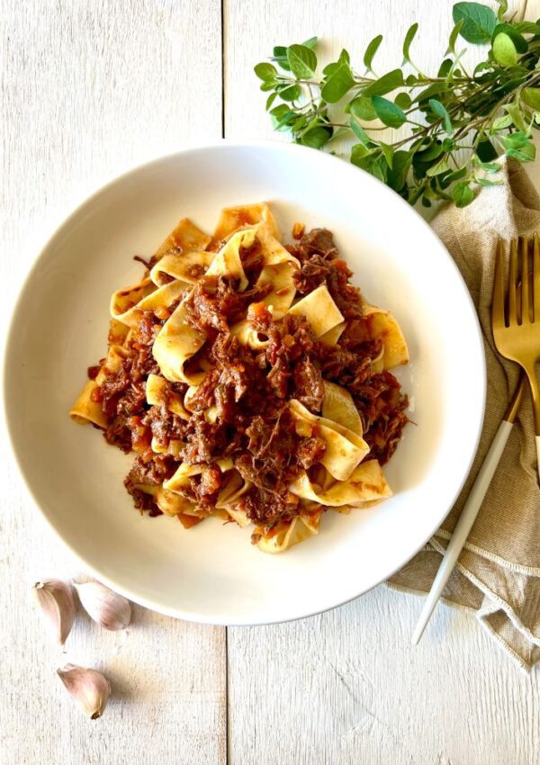 pasta with beef ragu in white bowl, white background, herbs and garlic